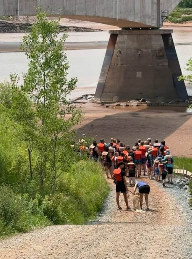 Visitors wearing life jackets walking down to the Shubenacadie River for a tidal bore rafting tour