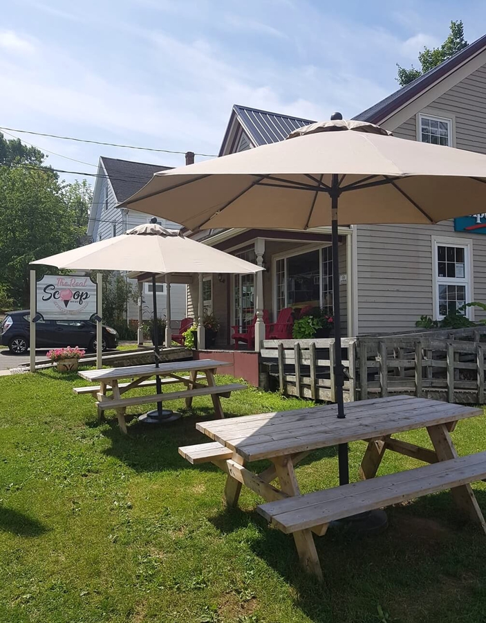 Outdoor seating area at The Real Scoop ice cream shop in Wolfville, Nova Scotia, with picnic tables and umbrellas on a sunny day